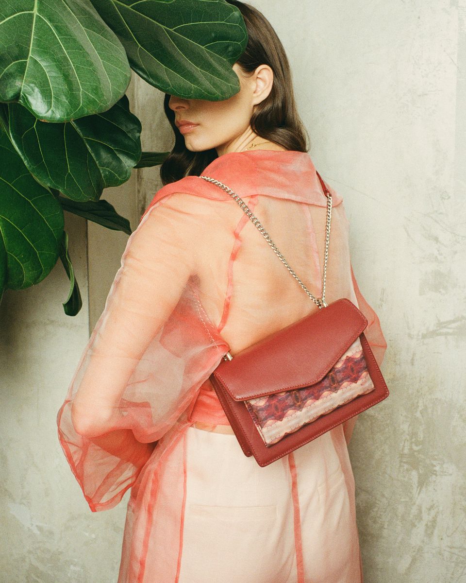 Model in a sheer coat carrying a red leather bag