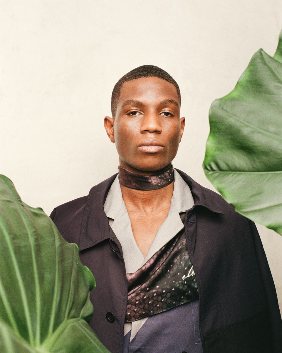 Model wearing a silk scarf with a dark coat among plants