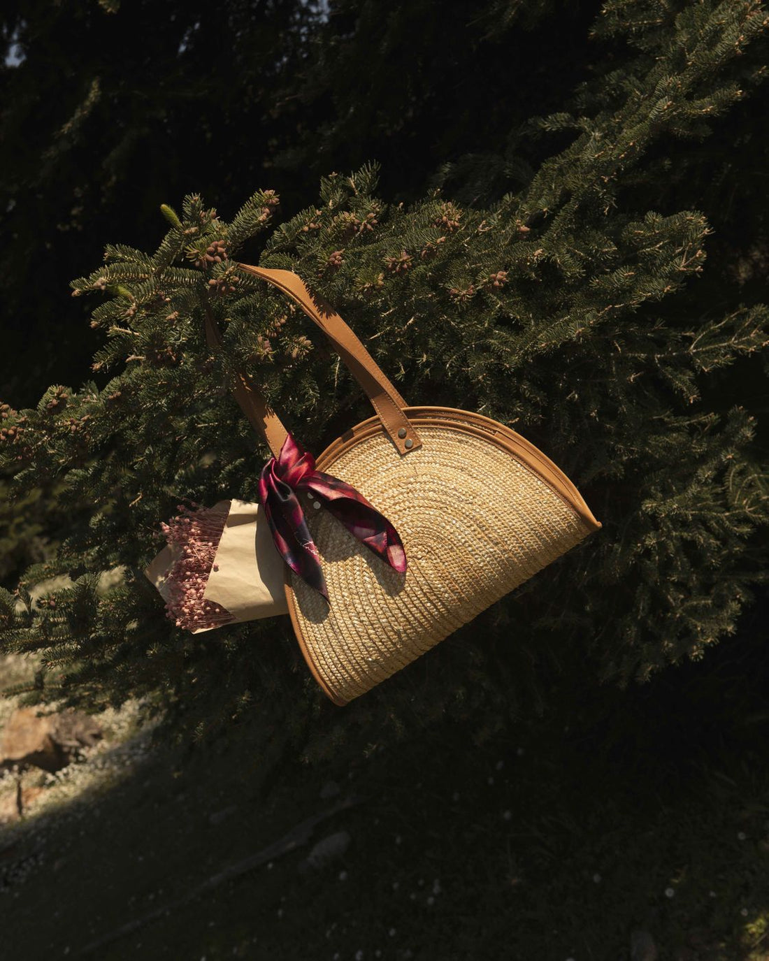 Woven bag with a silk scarf hanging in a pine tree