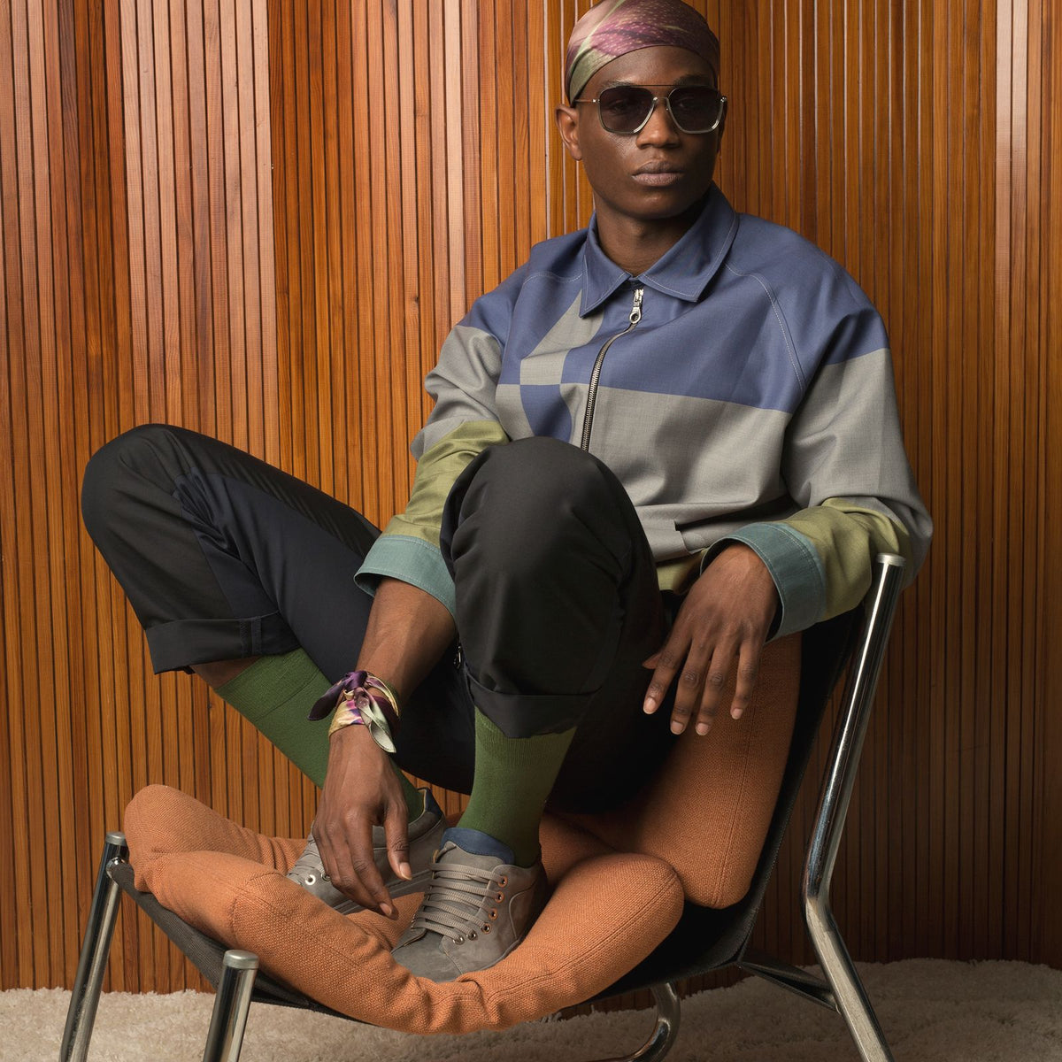 Model seated against warm wood panelling wearing silk accessories